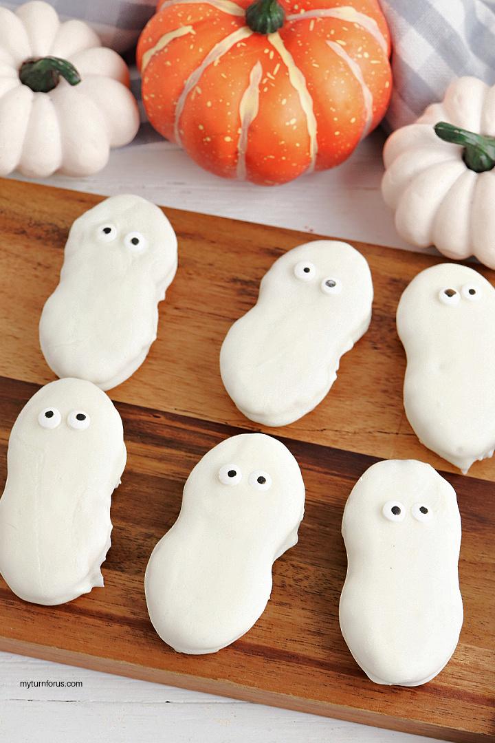 White chocolate covered Nutter Butter ghost cookies with small candy eyes arranged on a wooden serving board