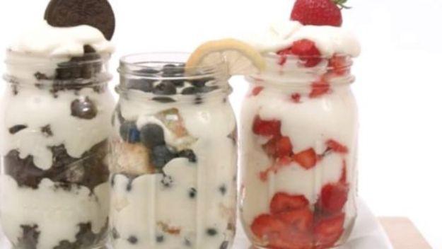 Three mason jars layered with whipped cream and cookie crumbs, blueberries and sliced strawberries on a white cloth