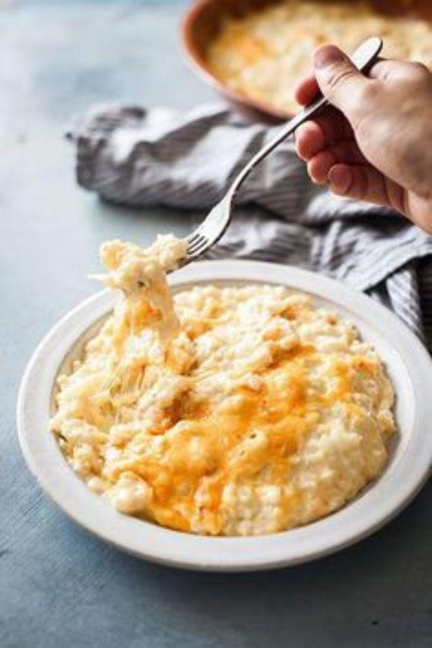 Keto cauliflower mac and cheese in a white bowl, a hand lifting a fork with a long stretch of melted cheddar