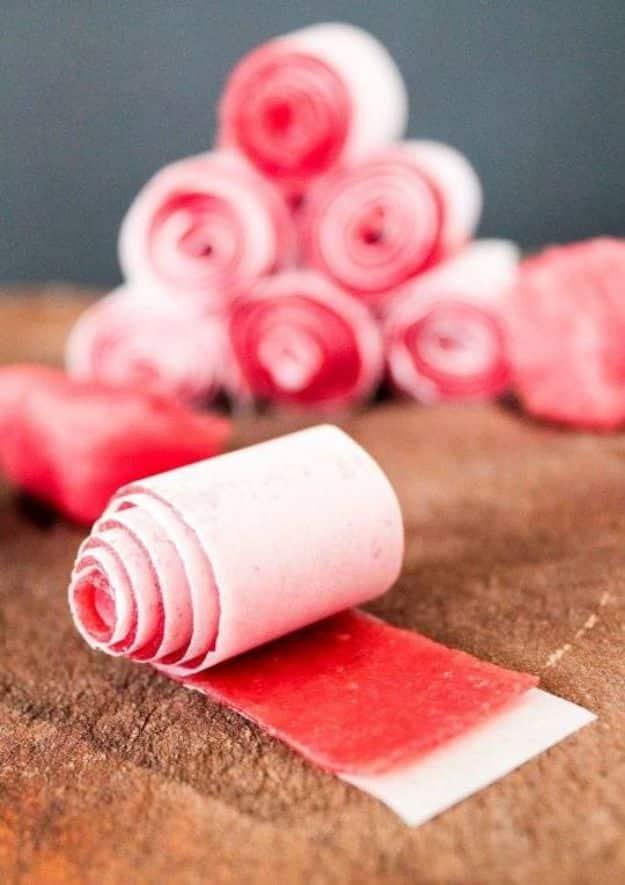 Watermelon fruit leather rolled into pink spirals with one strip unrolled flat on brown parchment paper