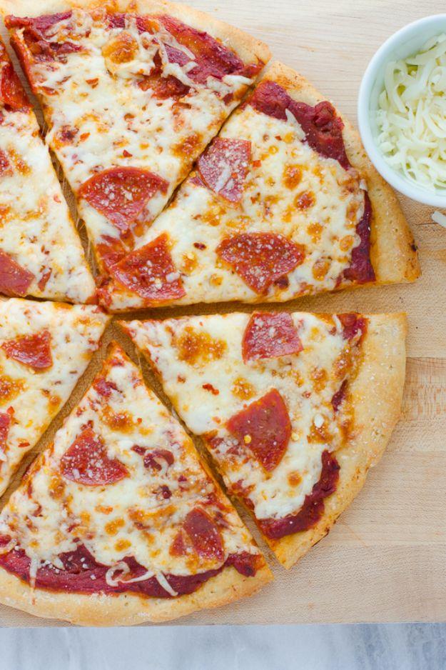 Gluten free pepperoni pizza cut into slices on a wooden board beside a white bowl of shredded mozzarella
