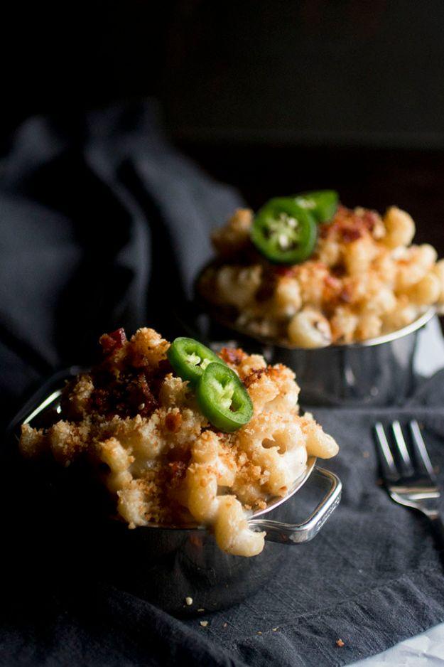 Jalapeno popper mac and cheese in two small handled metal pails on a dark cloth, topped with panko and peppers