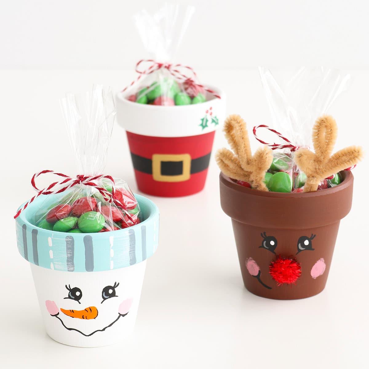 Mini terracotta pots painted as a snowman, Santa's belt and a reindeer with pipe cleaner antlers, each holding a bag of candy