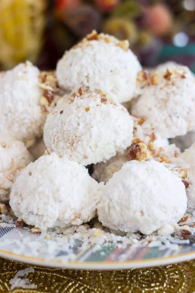Coconut pecan snowballs dusted in powdered sugar with chopped pecans on a patterned gold rimmed plate