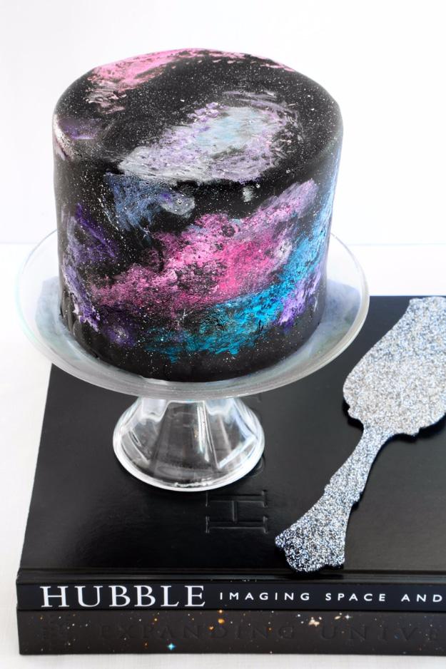 Black velvet nebula birthday cake painted with purple and pink galaxy swirls on a small glass cake stand