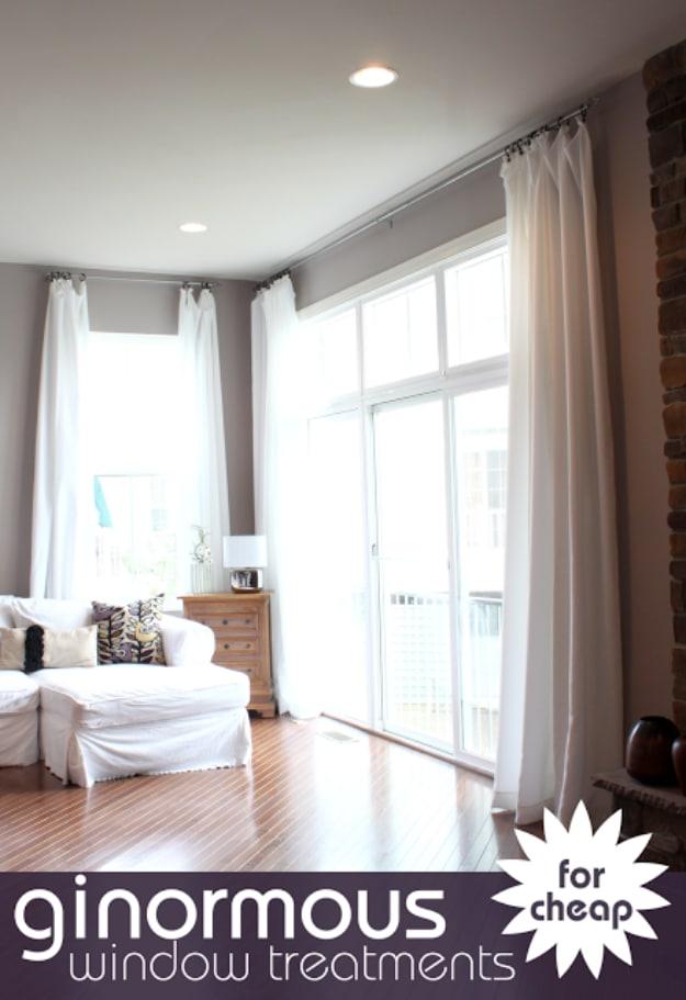 Extra long white curtain panels hanging ceiling height to floor at three windows in a bright white living room