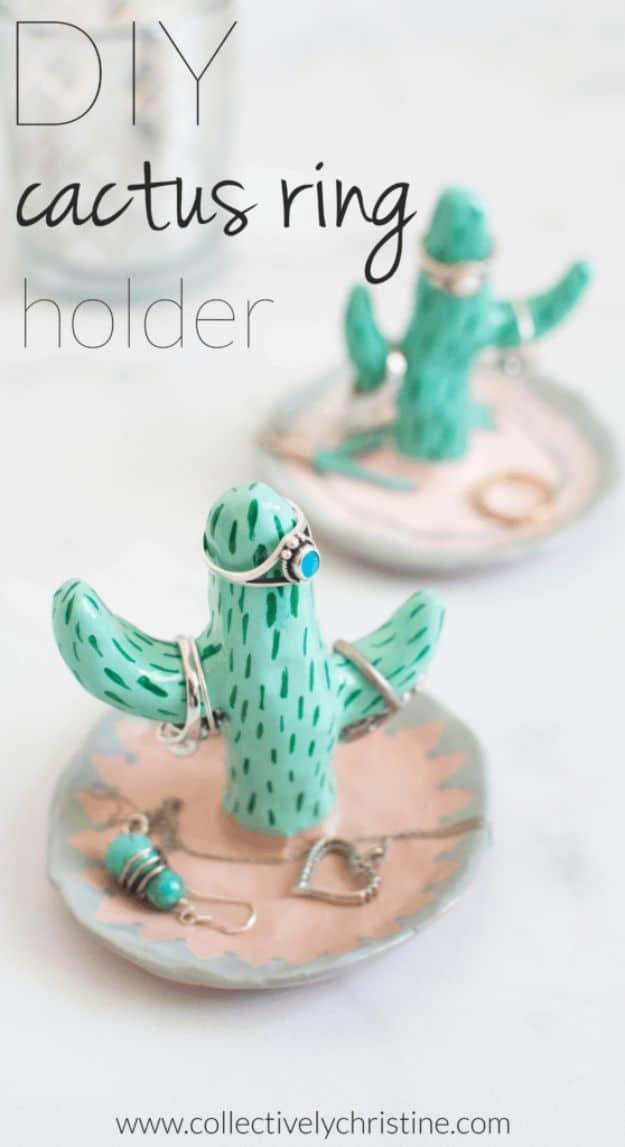 A little green clay cactus painted in two shades, sitting in a small pot of sand with gold rings hooked over its arms.