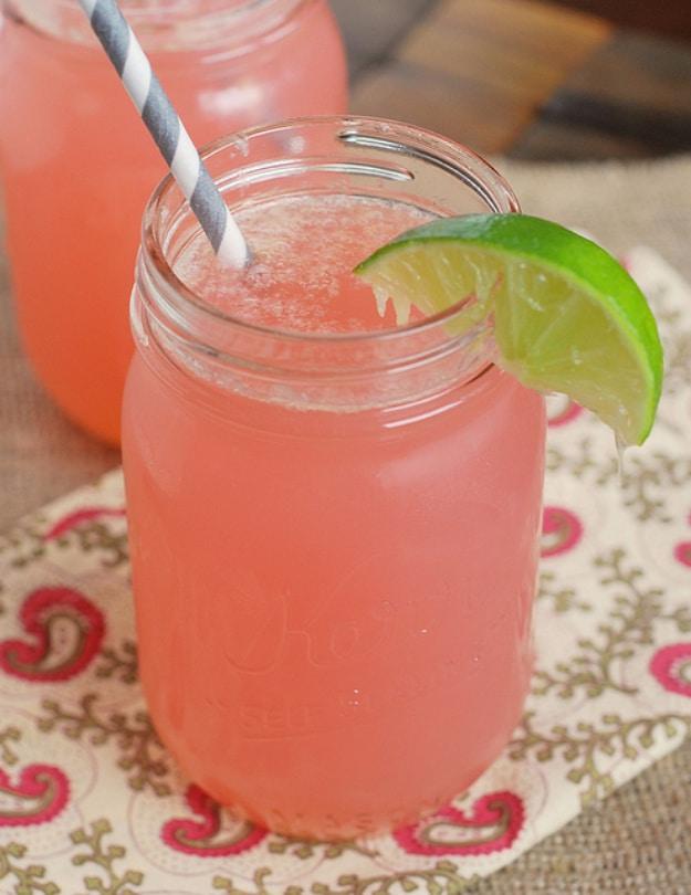 Two jars of pale pink cherry beergarita with a lime wedge and a striped paper straw on a paisley cloth