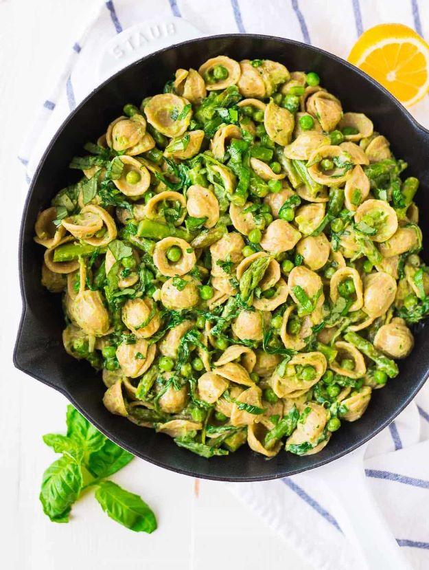 Creamy avocado pasta with asparagus and peas in a black skillet, orecchiette coated in bright green sauce