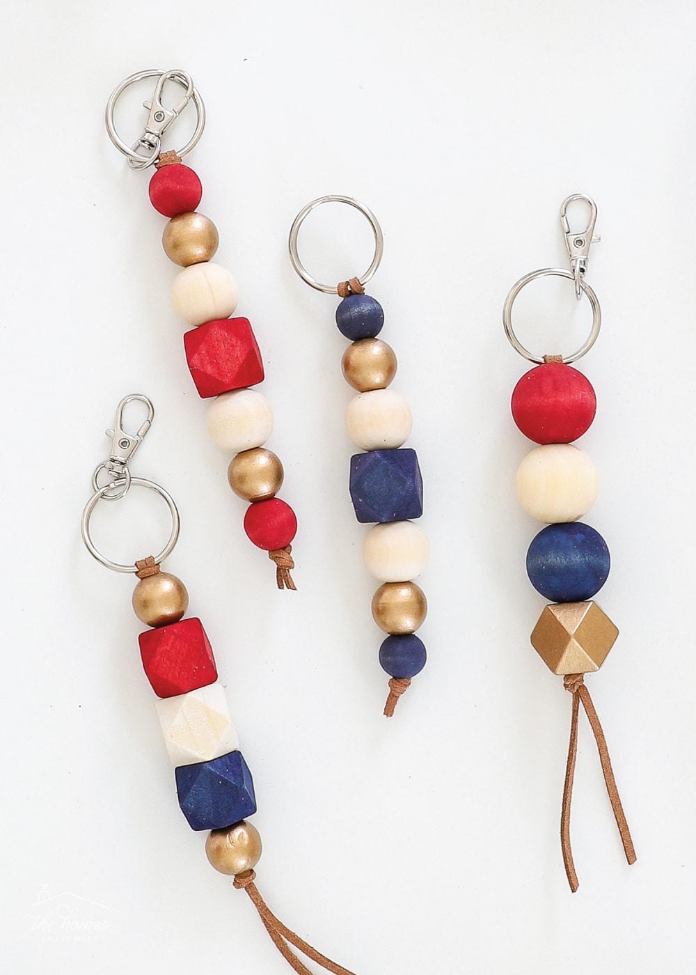 Four wood bead keychains on silver rings with navy, red, gold and natural beads and leather tassels on a white background