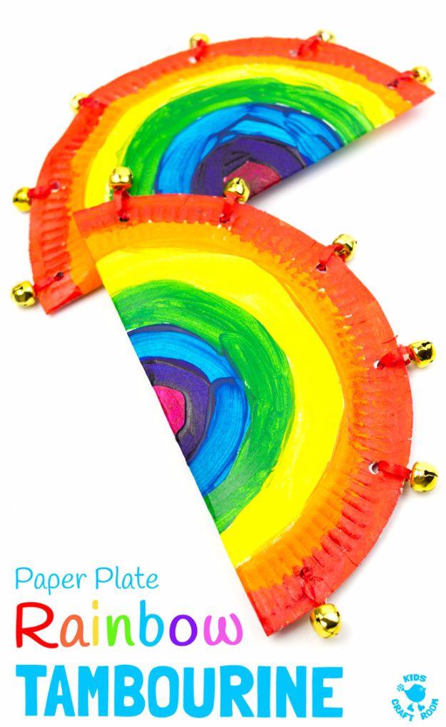 Two rainbow painted paper plate tambourines folded in half with gold jingle bells tied around the curved edges