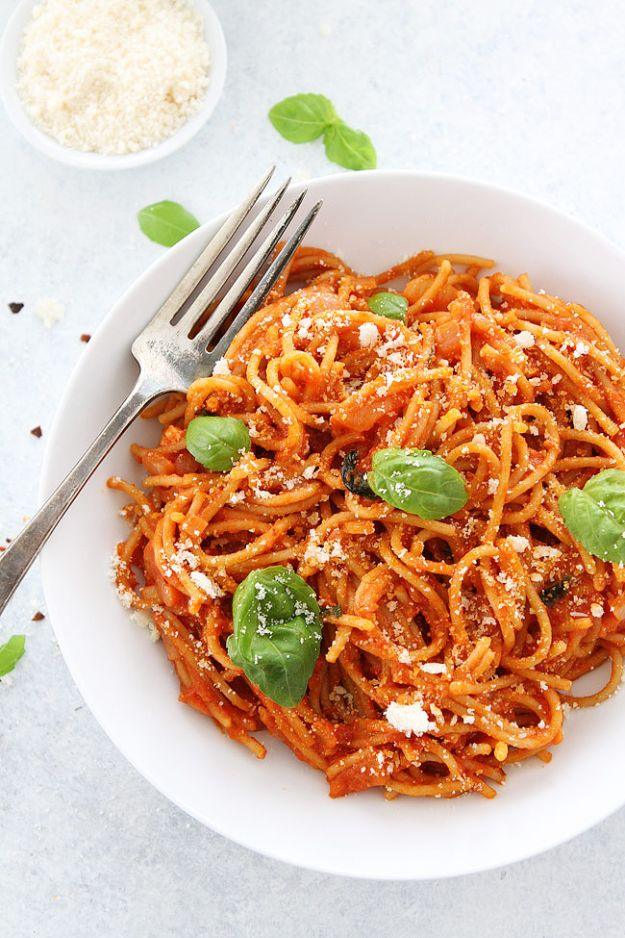 Pasta pomodoro, spaghetti in a red tomato sauce on a white plate with fresh basil leaves and grated parmesan