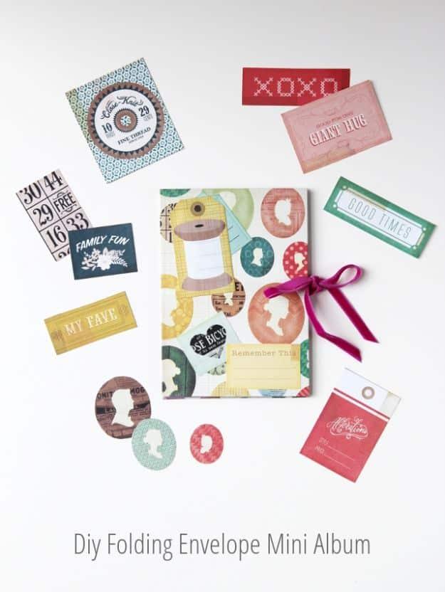 Folding envelope mini album with a patterned cover and pink ribbon, surrounded by cut paper tags on white