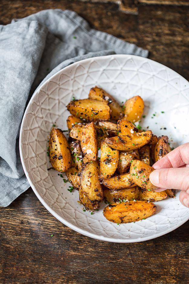 White bowl of crisp browned chipotle potato wedges with a hand lifting one out, dark wooden table below