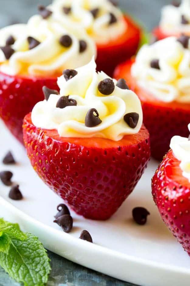 Cheesecake stuffed strawberries topped with piped white filling and mini chocolate chips on a white plate