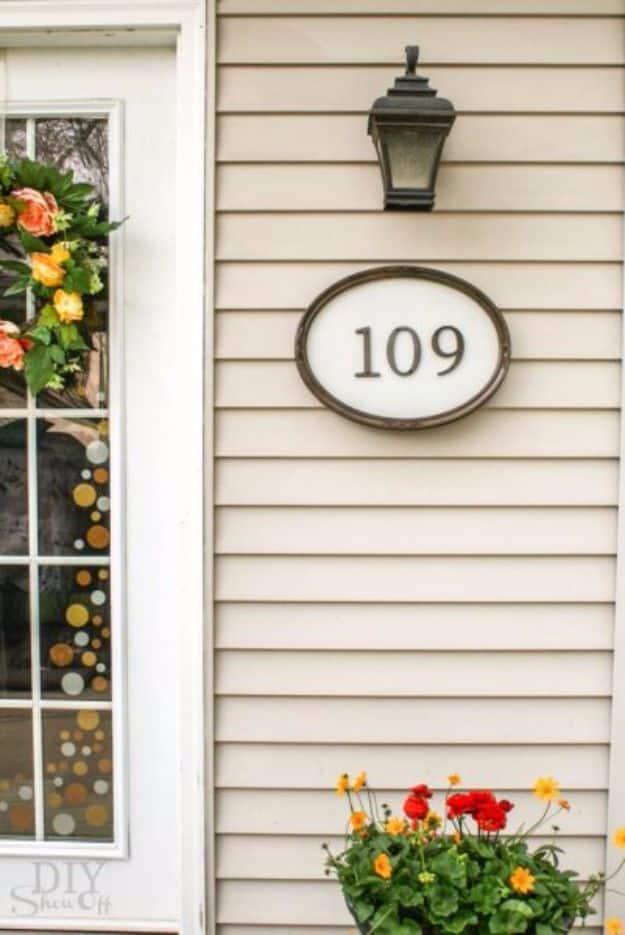 Oval framed house number sign with 109 in dark numerals, mounted on cream siding above red geraniums