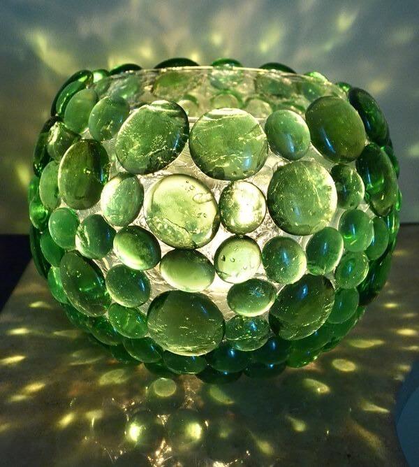 A round glass candle holder covered in rows of green glass gems, glowing with a candle inside and casting green light