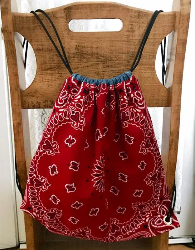 DIY bandana backpack, a red paisley drawstring bag with black paracord straps hanging on a wooden chair