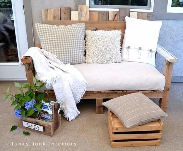 Pallet wood loveseat with a cream cushion, gingham pillows and a white throw, beside a wooden crate side table