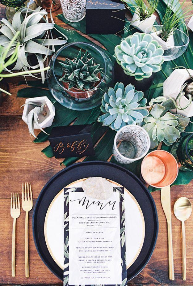 Dark green table runner with succulents and air plants, a black charger, printed menu card and gold flatware