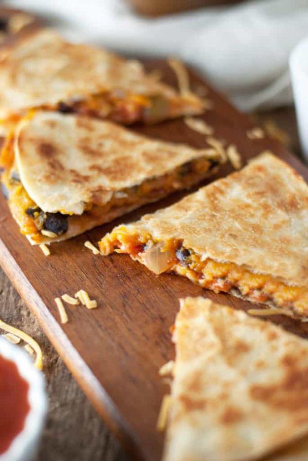 Black bean and butternut squash quesadillas cut into wedges on a wooden board with melted cheese showing