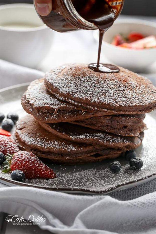 Double chocolate brownie pancakes dusted with powdered sugar with chocolate sauce poured over the stack