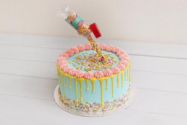 Pastel gravity cake with a candy tube suspended above it pouring sprinkles down over the drip frosting