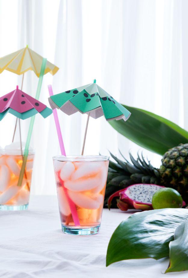 Three folded paper cocktail umbrellas as watermelon, kiwi and lemon slices, propped in iced drinks with a pineapple