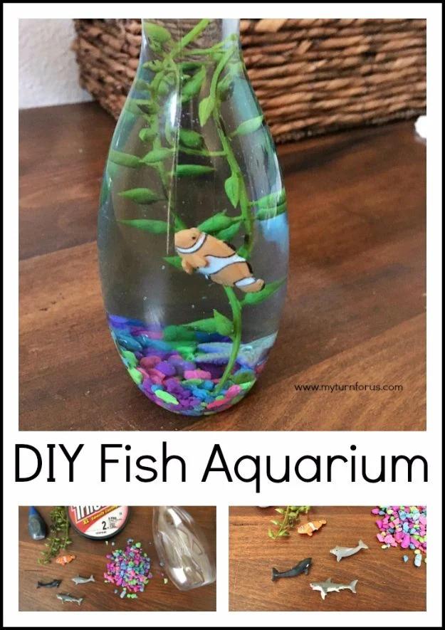 DIY aquarium in a plastic bottle with a clownfish on fishing line, green plants and purple gravel on a table