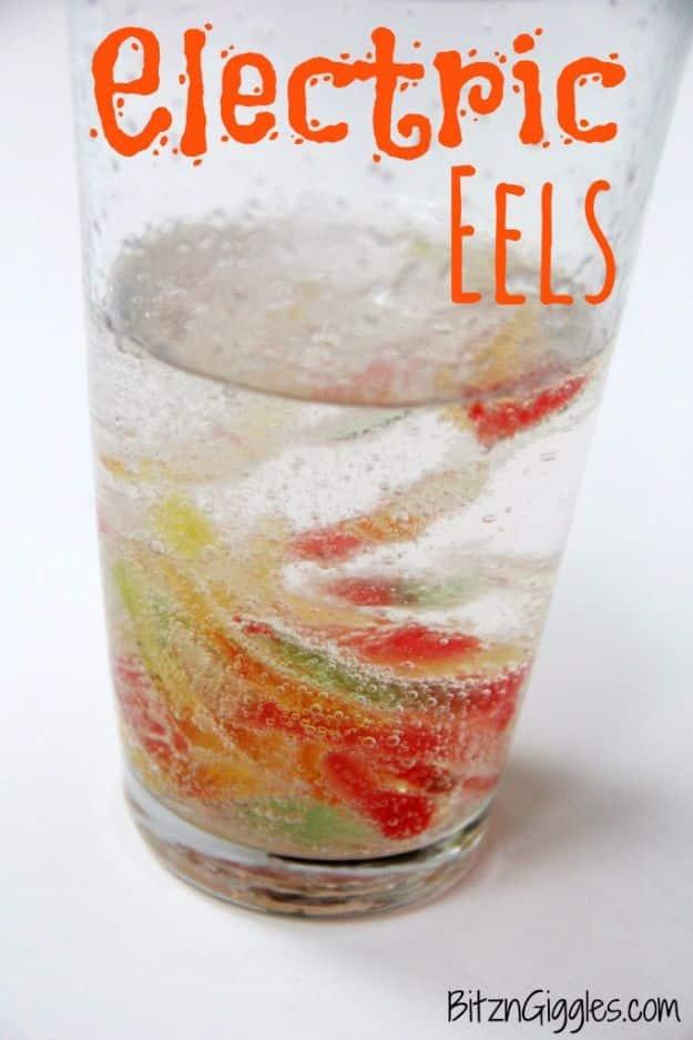 Electric eels, red and yellow gummy worm pieces jumping and twisting in a tall glass of fizzing clear vinegar