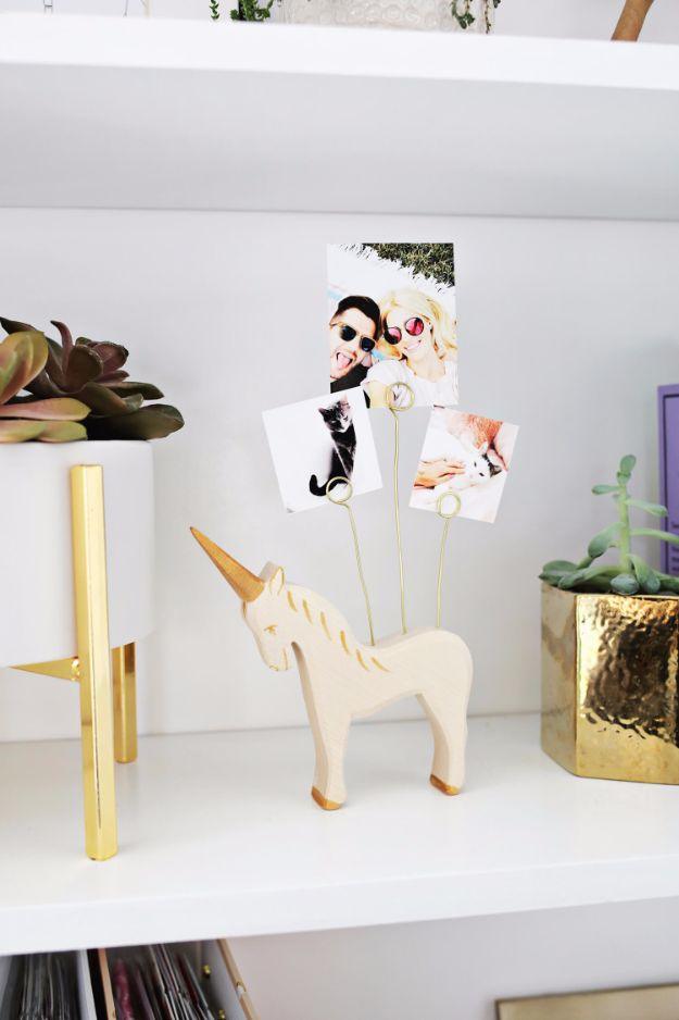 Small wooden unicorn with gold tipped horn and hooves holding three photos on curled brass wires on a white shelf