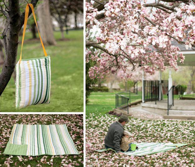 All in one picnic blanket tote, a green striped blanket folded into its own shoulder bag hanging from a tree in a park
