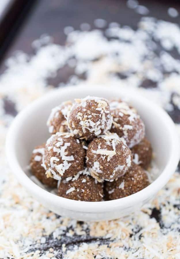 Coconut date balls dusted with shredded coconut piled up in a small white ramekin on a dark wood surface