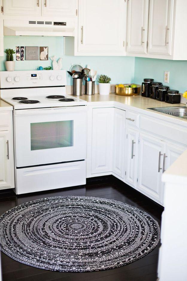 Round coiled DIY rope rug in black, white and grey fabric on a dark floor in a white kitchen by the oven