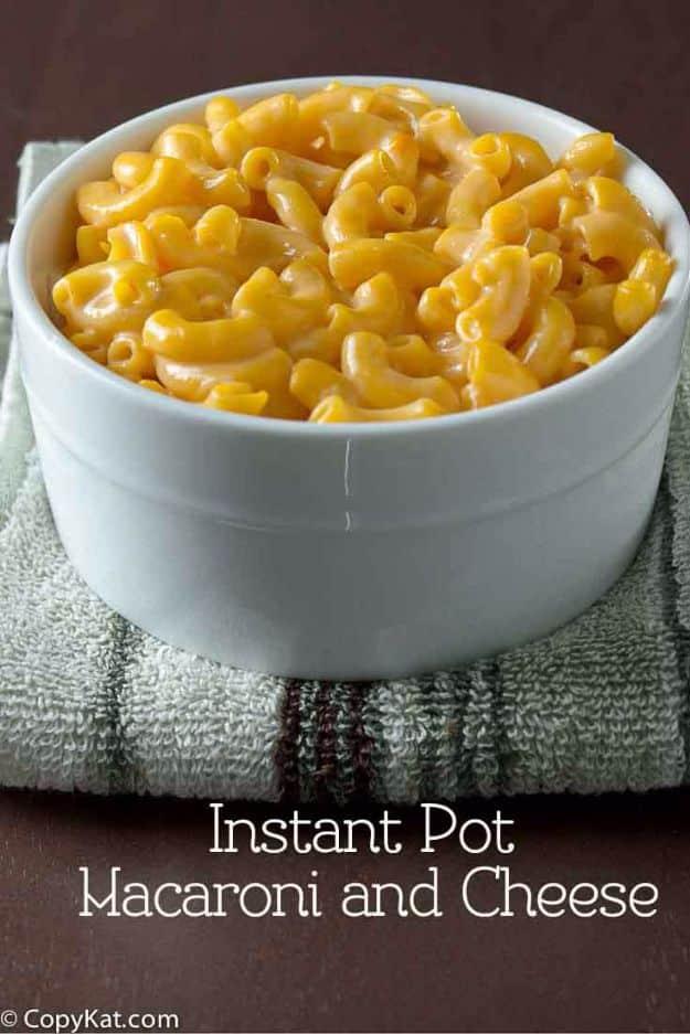 Graphic reading Instant Pot Macaroni and Cheese under a white bowl of creamy elbow macaroni on a folded grey towel