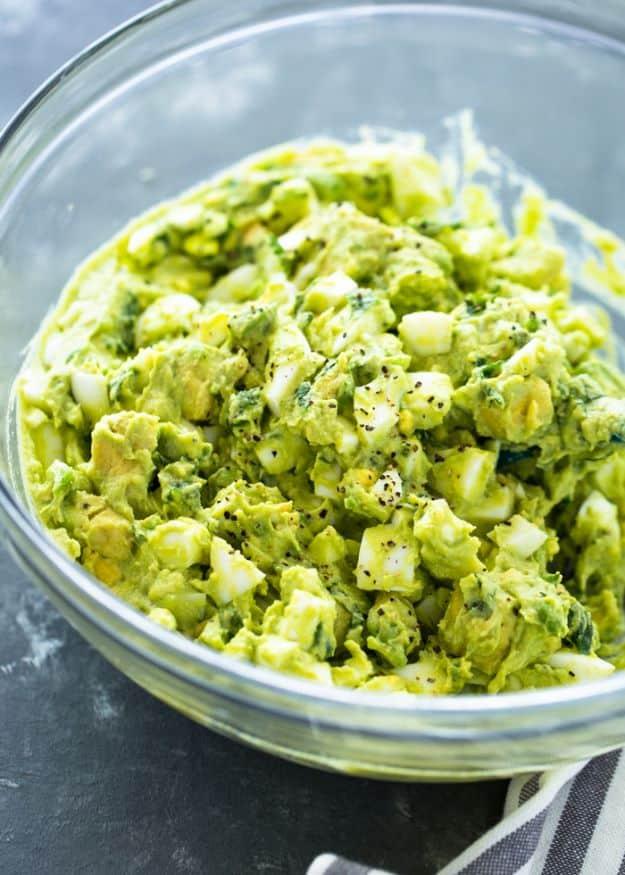 Creamy avocado egg salad, a glass bowl of pale green chopped egg and avocado salad flecked with fresh herbs