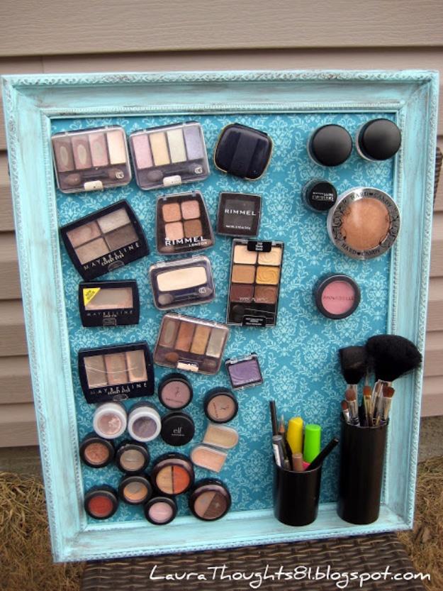 Make up magnet board, a teal framed fabric board covered in magnetized eyeshadow palettes and brushes