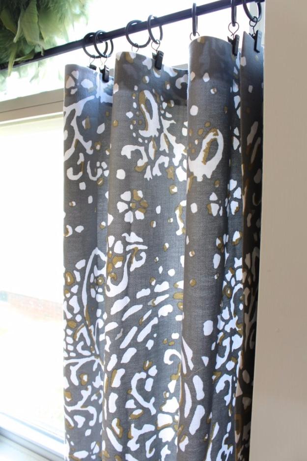DIY cafe curtains in grey and gold print fabric hanging from black clip rings on a rod, seen close up against a window