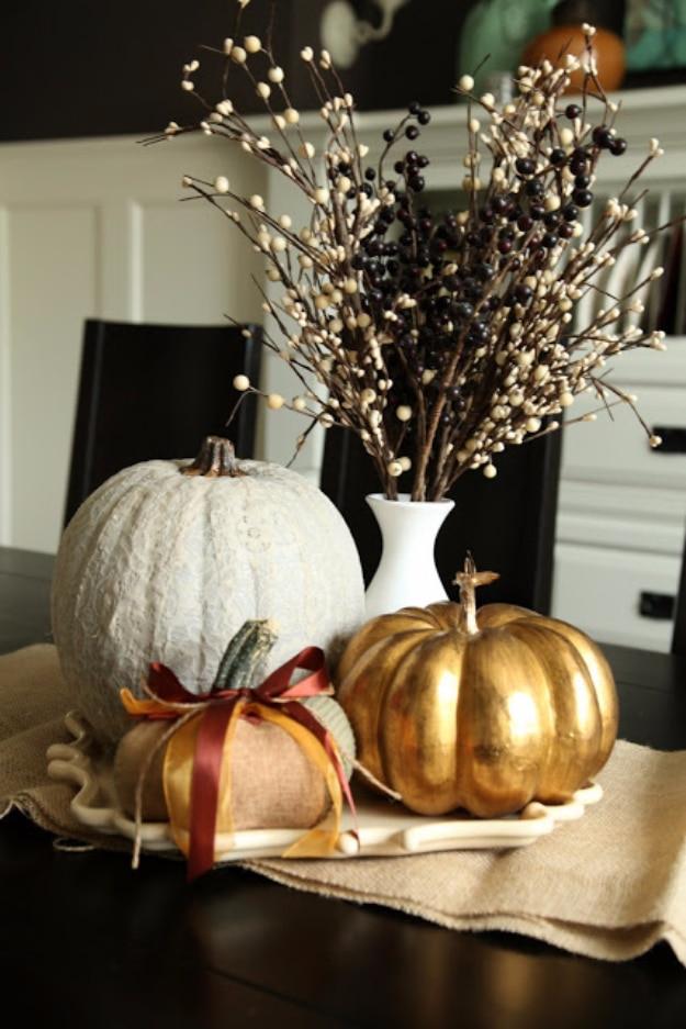 Gray and white lace covered pumpkin beside a gold painted pumpkin and a burlap pumpkin with a red bow