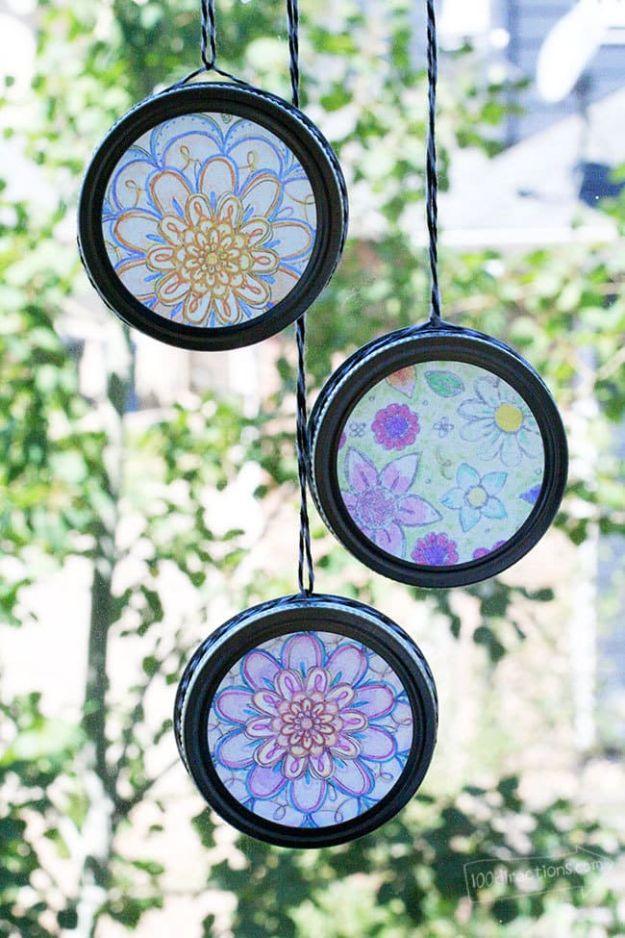 Three colored mandala suncatchers mounted in black mason jar bands, hanging on twine in front of green leaves