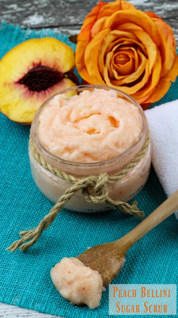 Peach bellini sugar scrub in a jar with a wooden spoon, a fresh peach and an orange rose on teal fabric
