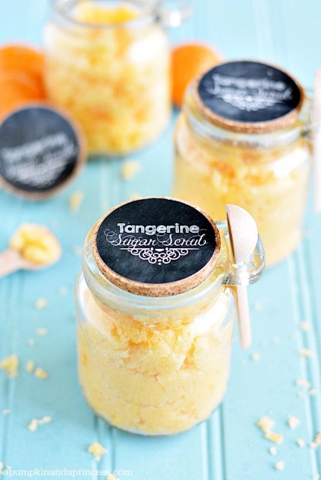 Coconut tangerine sugar scrub in three jars with black chalkboard lids, a wooden spoon and scattered zest