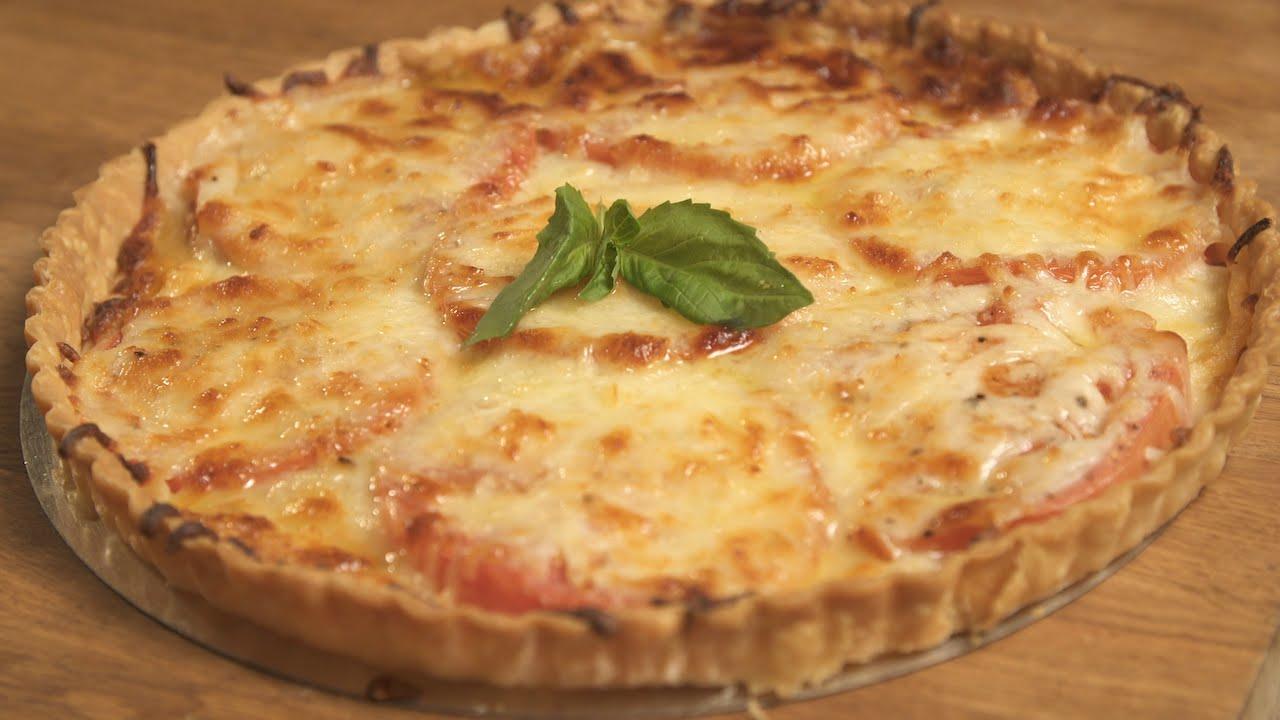 Round southern tomato pie in a fluted tart pan with a browned cheese topping and a basil leaf on top