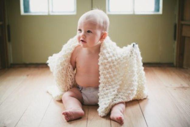 Thick cream chunky knit baby blanket with very large stitches, held by a baby sitting on a wooden floor