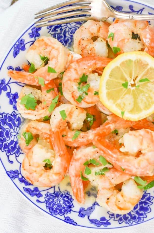 Garlic butter shrimp on a blue and white patterned plate with a lemon slice and chopped green onion on top