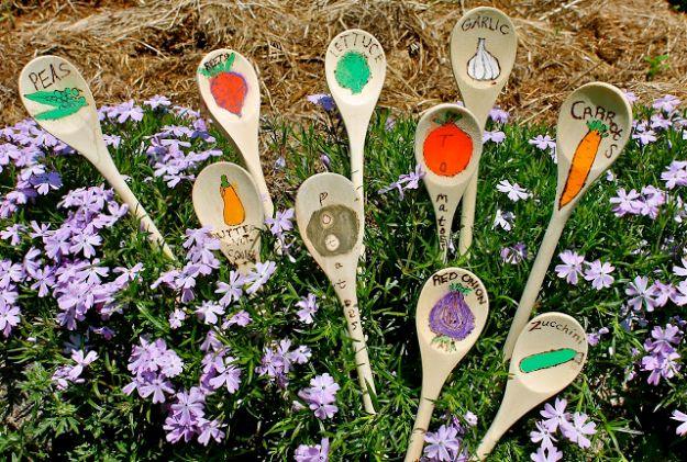 Ten painted wooden spoons labelled peas, garlic, carrots and more, pushed upright into a garden bed of purple phlox