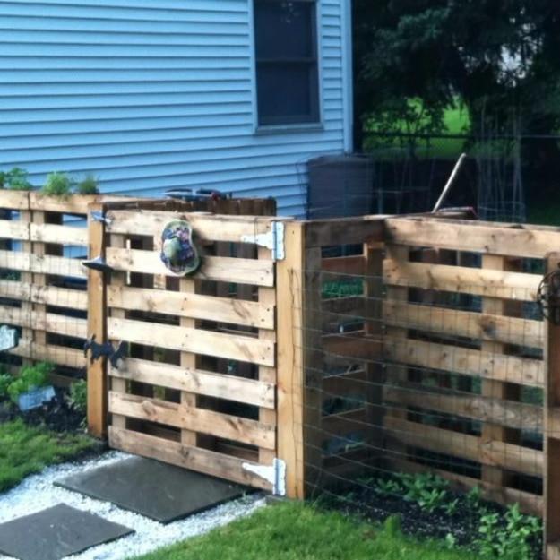 Amazing DIY pallet fence, a wooden pallet fence and gate with black hinges beside a blue sided house and a gravel path