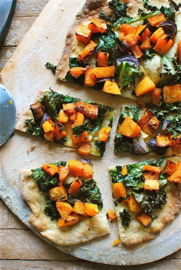 Roasted butternut squash and kale pizza on a wooden board cut into slices with orange squash and green kale