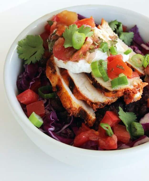 Healthy burrito bowl with rice, black beans, sliced chicken, salsa, cheese and fresh vegetables in a bowl