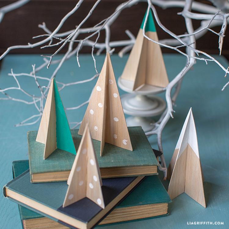 Five small balsa wood slot together trees painted with white polka dots and teal or white tops on a stack of old books